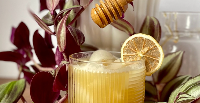 Honey drizzling from a dipper into a citrus mocktail garnished with a dried lemon wheel