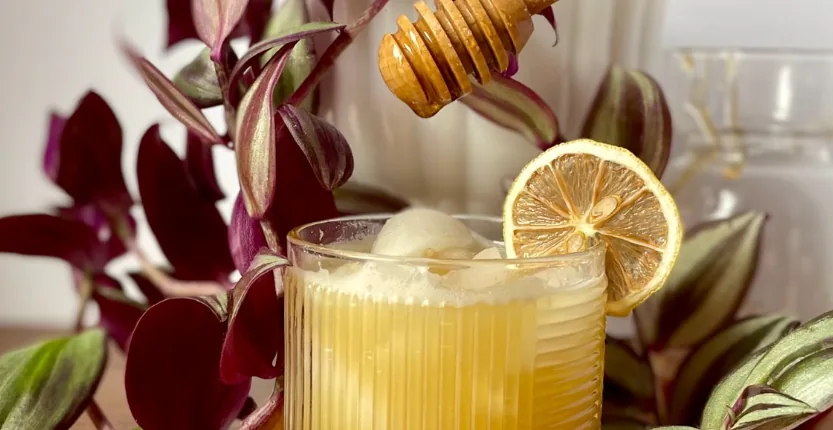 Honey drizzling from a dipper into a citrus mocktail garnished with a dried lemon wheel