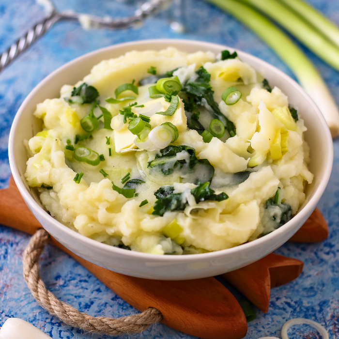 Bowl of colcannon mashed potatoes flecked with kale, leek and sliced scallions on a blue table