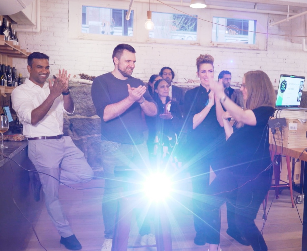 Colleagues clapping and cheering during a live team event in a brick-walled loft space
