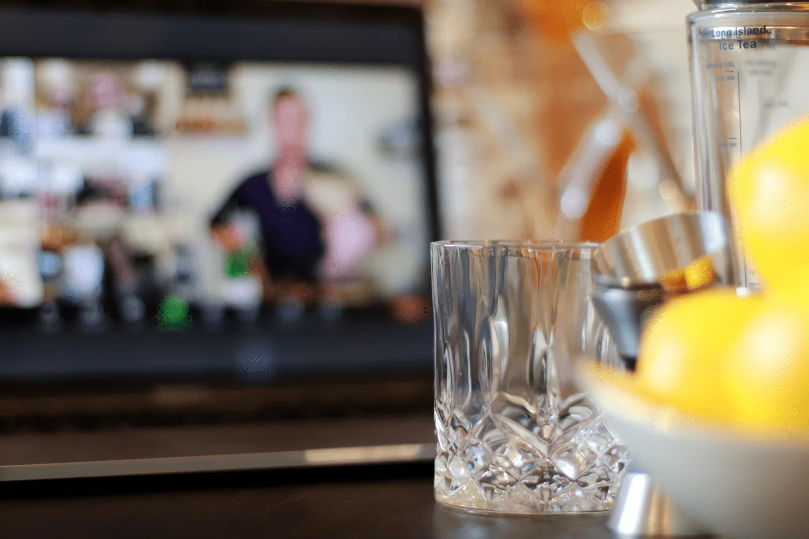 Crystal rocks glass and bar tools in front of a laptop streaming a live mixology host