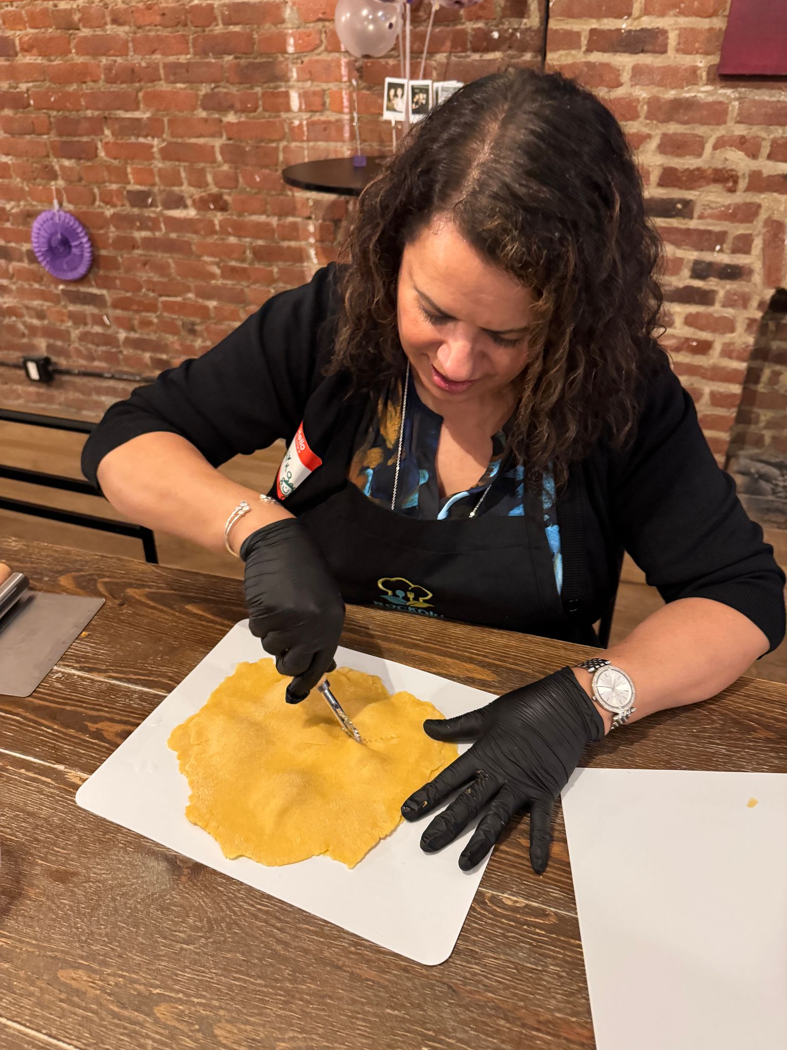 Guest in a black apron and gloves cutting a sheet of fresh yellow pasta dough on a white board