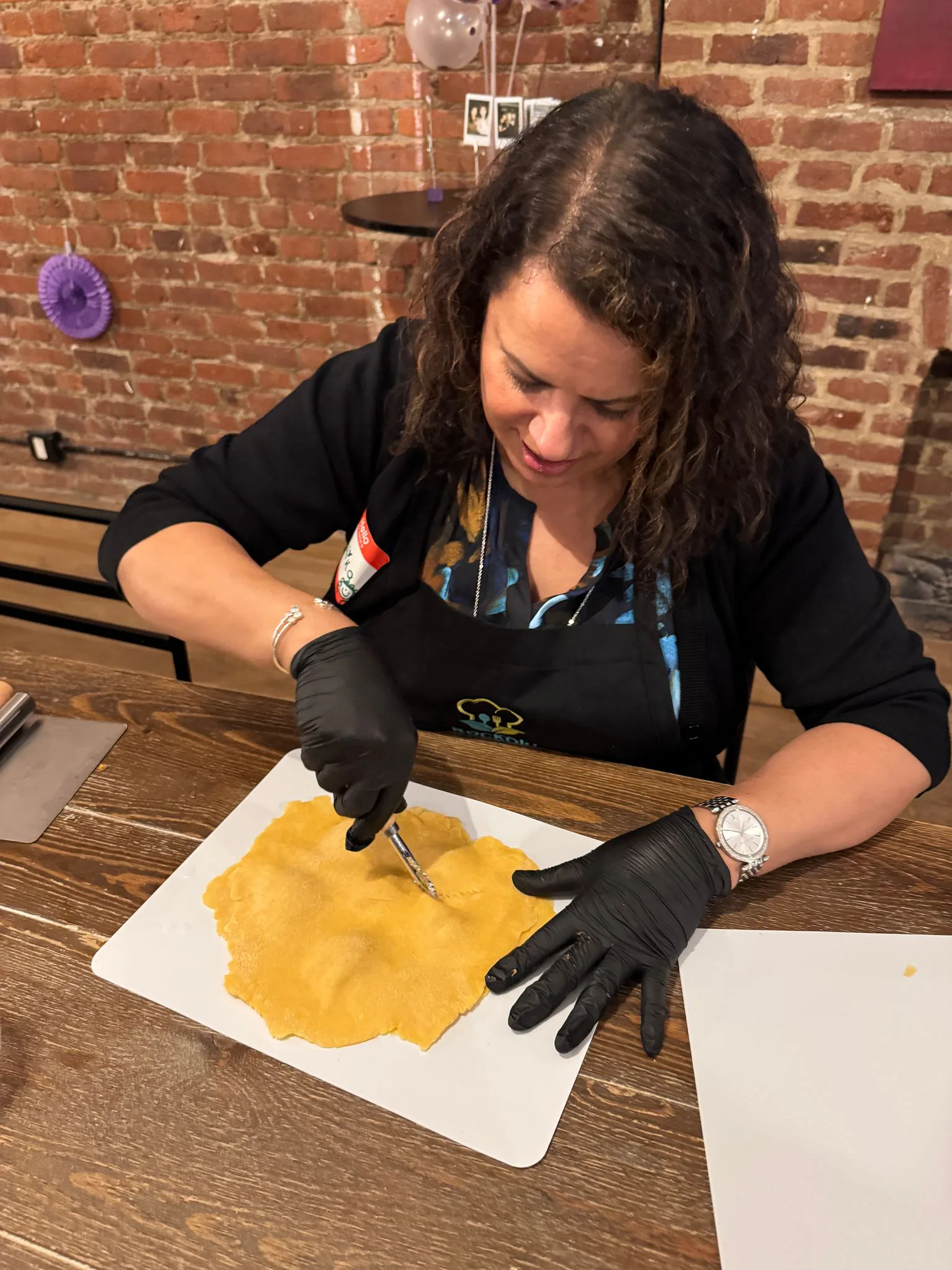 Guest in a black apron and gloves cutting a sheet of fresh yellow pasta dough on a white board