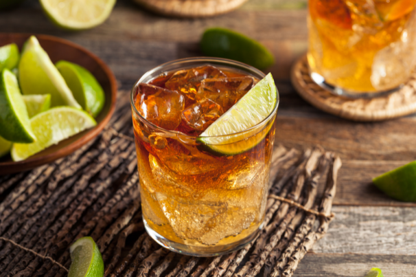 Dark drink layered over ice in a rocks glass with a lime wedge, next to a bowl of cut limes