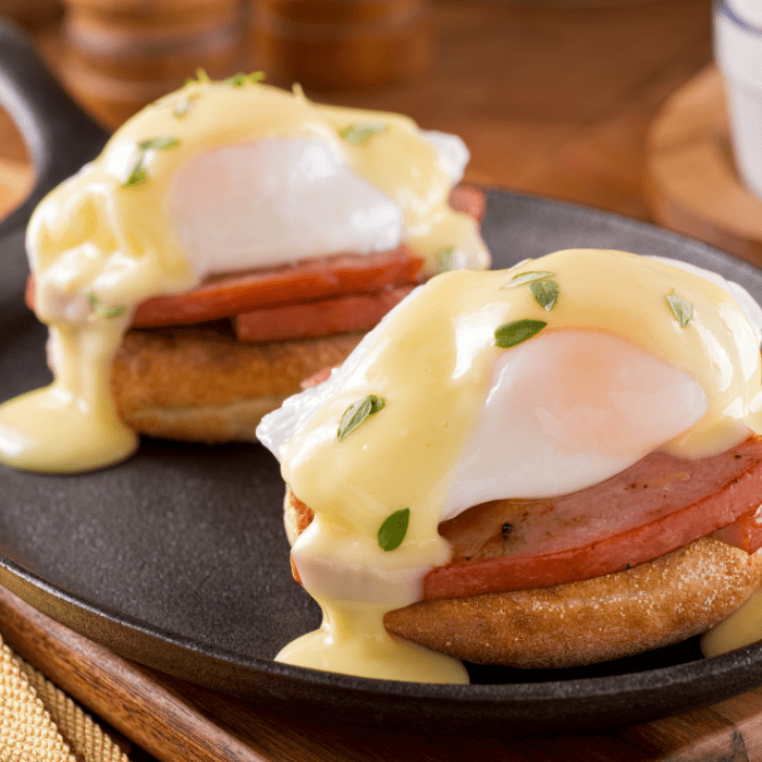 Two eggs Benedict on English muffins with ham and hollandaise sauce in a black cast-iron pan