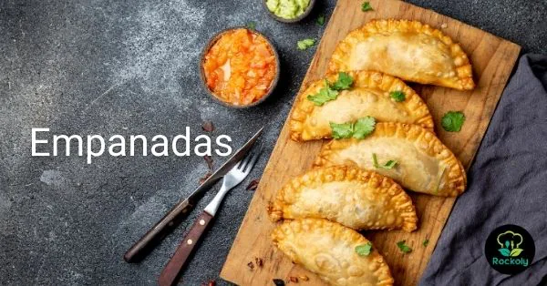 Banner reading Empanadas, with baked empanadas on a wooden board beside salsa and guacamole