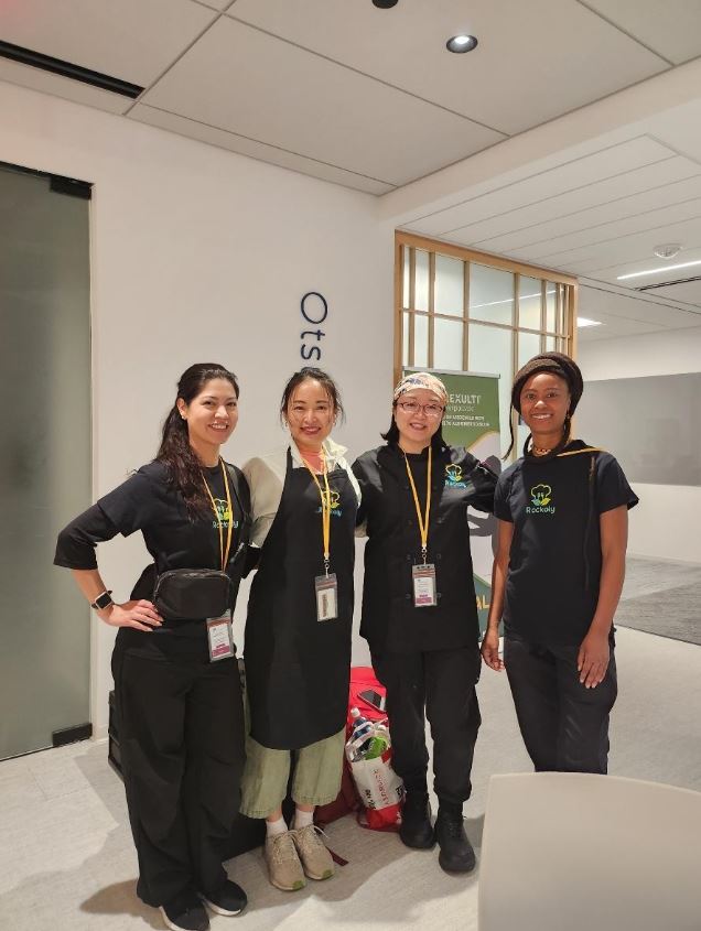 Four event staff in black aprons and lanyards smiling together in an office lobby