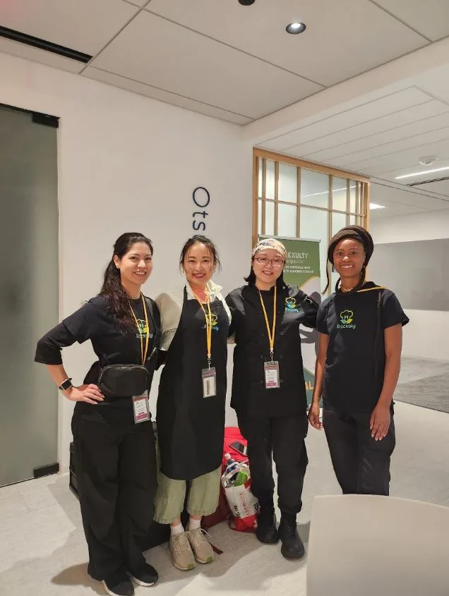 Four event staff in black aprons and lanyards smiling together in an office lobby