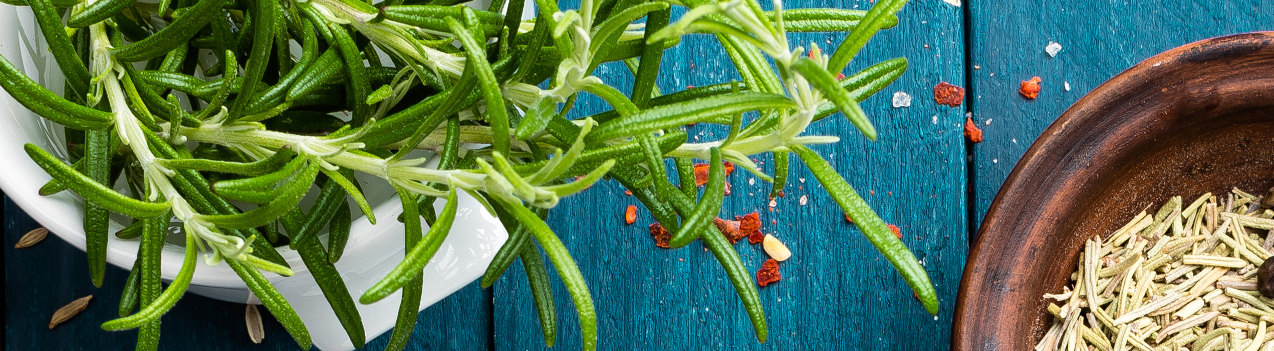 Fresh rosemary sprigs, pink peppercorns and whole spices scattered on a blue wooden table