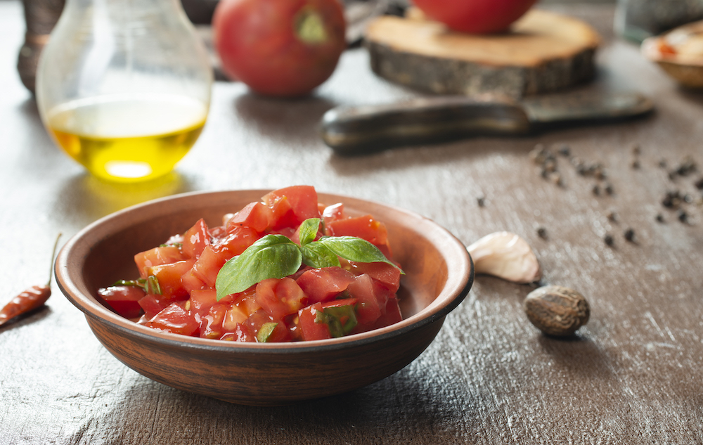 Rustic bowl of chopped tomato salsa topped with basil, with olive oil and garlic nearby