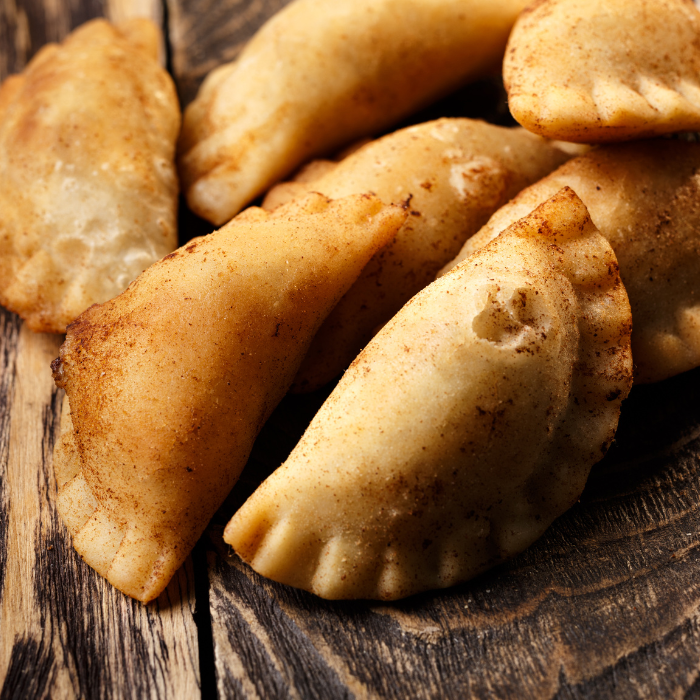 A pile of golden fried half-moon dumplings dusted with cinnamon sugar on a rustic wood board