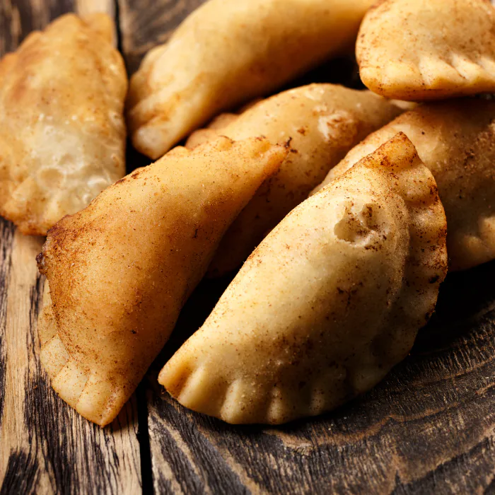 A pile of golden fried half-moon dumplings dusted with cinnamon sugar on a rustic wood board