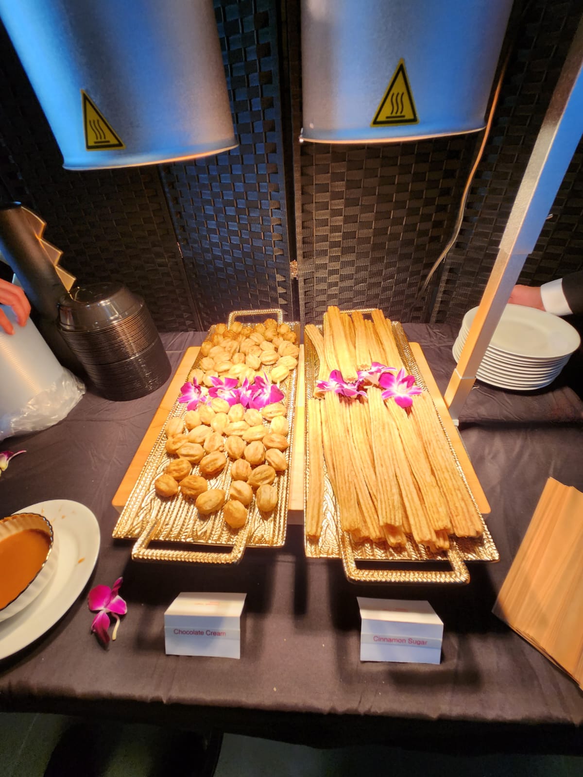 Gold buffet trays of fried dumplings and crisp pastry sticks garnished with orchids beside dipping sauce