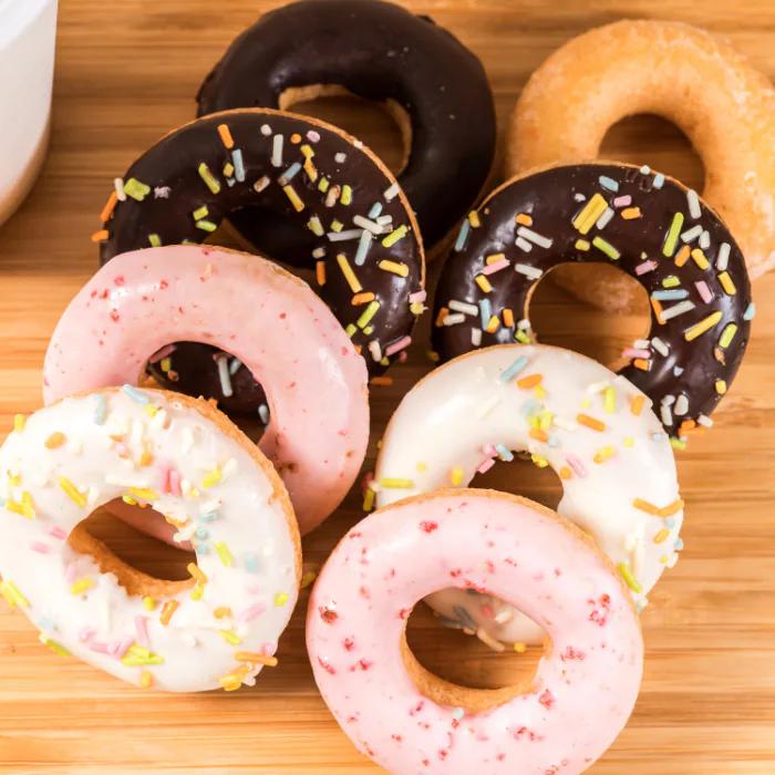 Pile of cake donuts with chocolate, pink and vanilla frosting and rainbow sprinkles on a wooden board