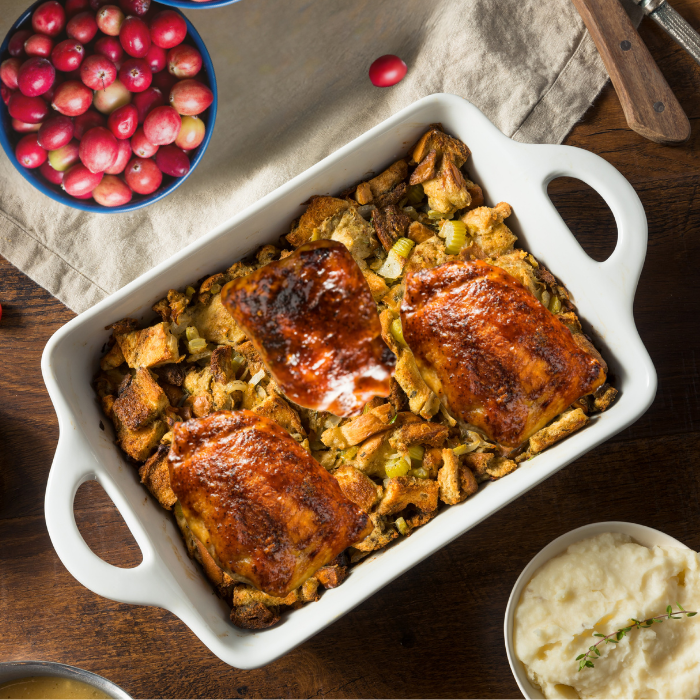 Glazed chicken pieces baked over bread stuffing in a white dish, with cranberries and mashed potatoes