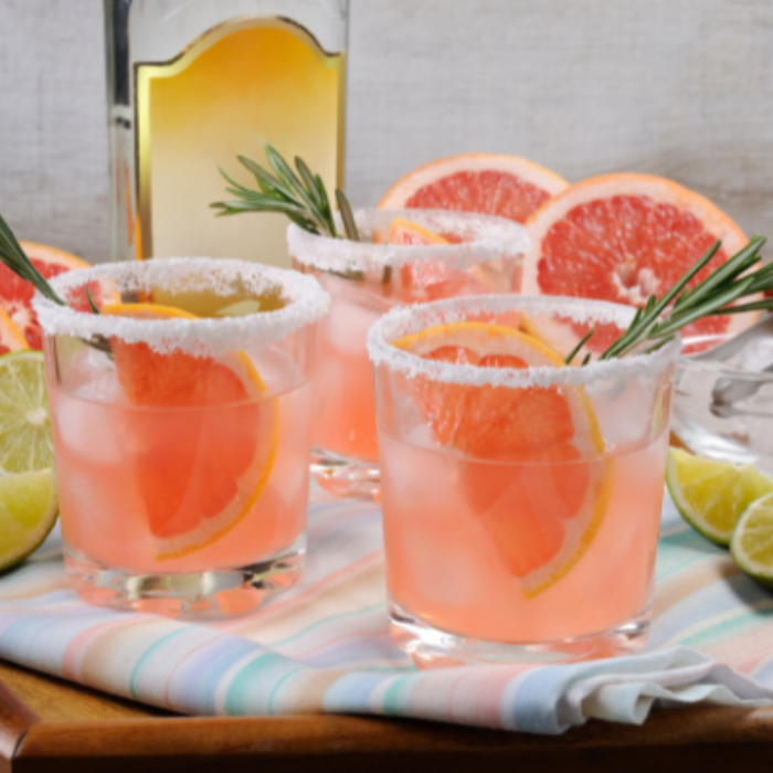 Three grapefruit cocktails with salted rims and citrus slices on a striped cloth