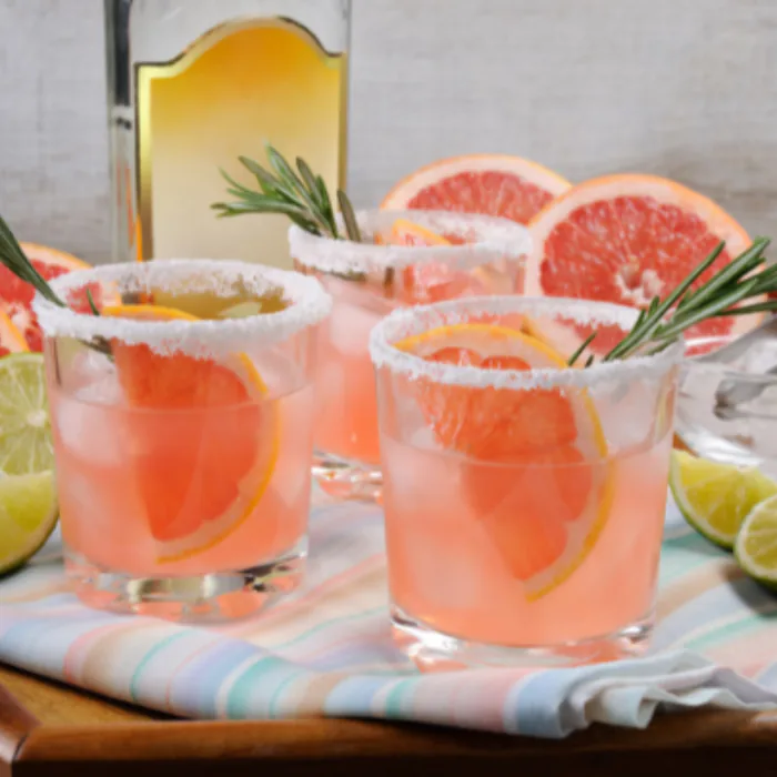 Three grapefruit cocktails with salted rims and citrus slices on a striped cloth
