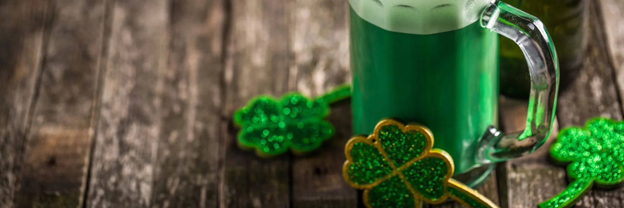 Mug of green beer on rustic wood surrounded by glittery green shamrock decorations