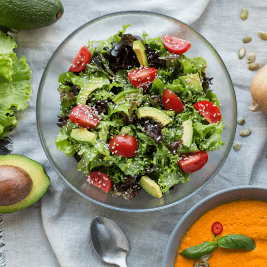 Leafy green salad with avocado and cherry tomatoes beside a bowl of creamy orange soup