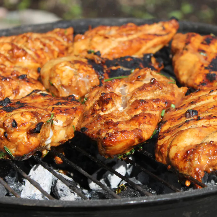 Charred pieces of grilled chicken cooking over glowing coals on a round charcoal grill