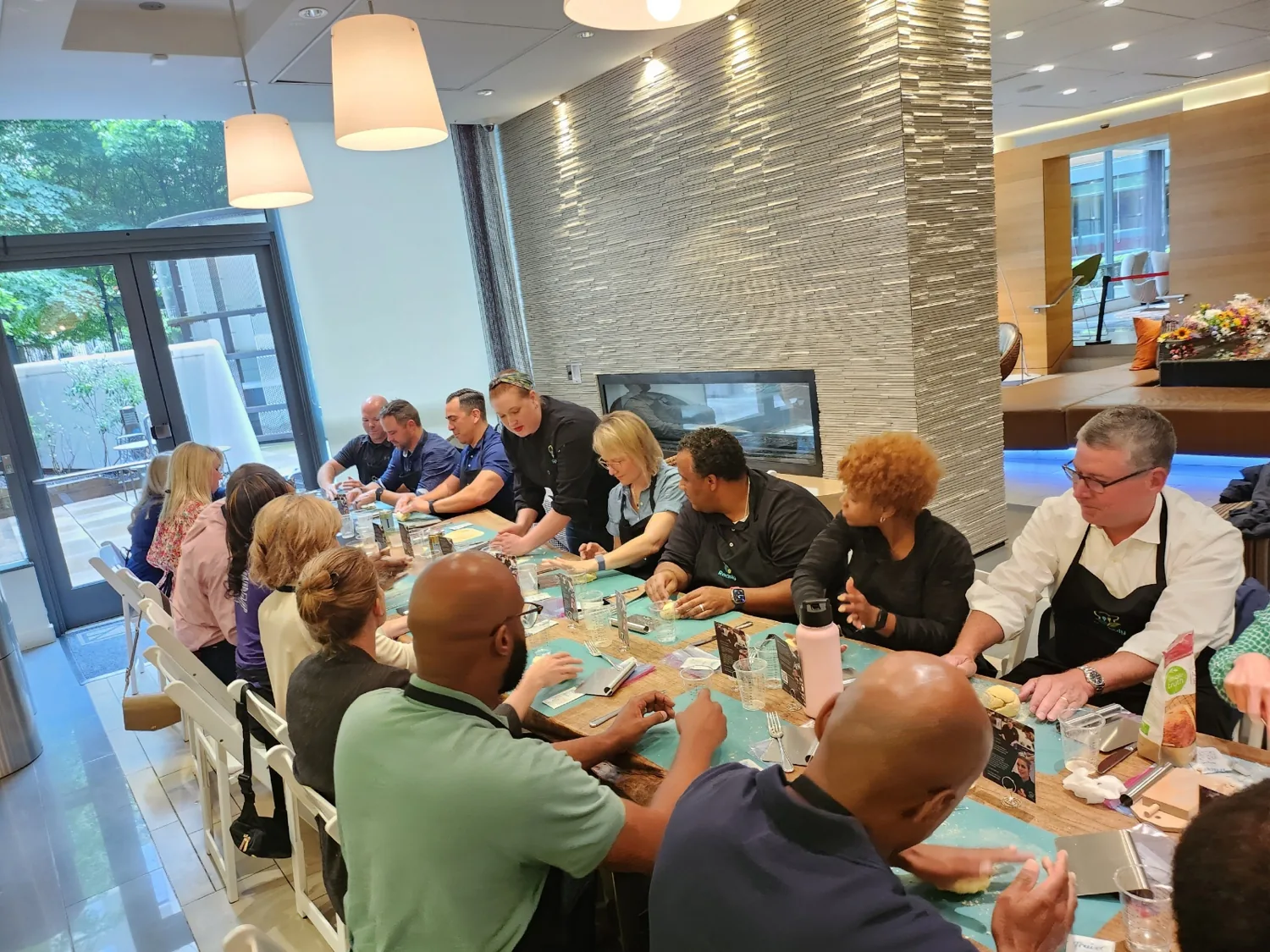 Guests seated along a long communal table in aprons working through a hands-on cooking class