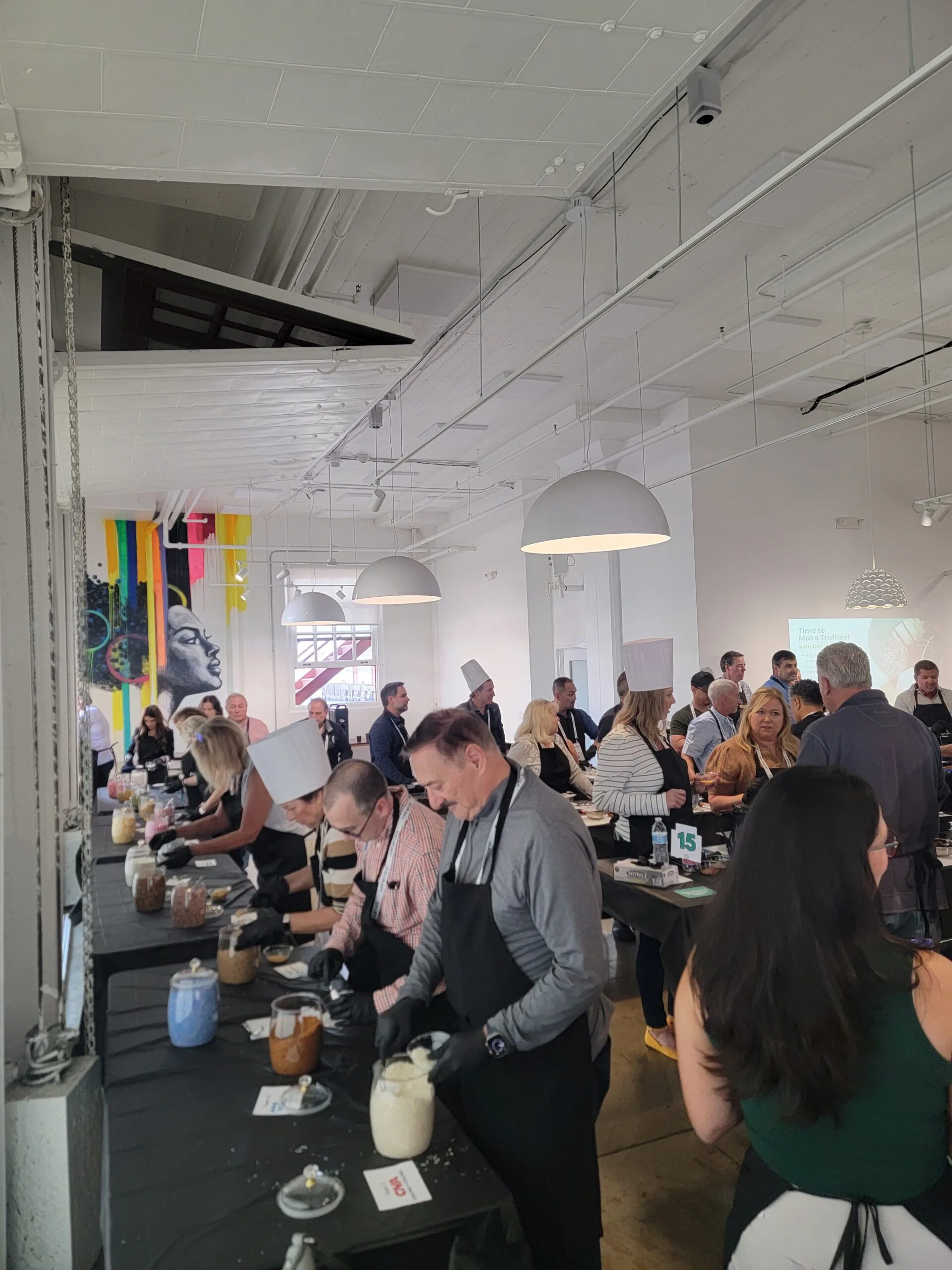 Guests in aprons working along rows of prep tables during a hands-on event in a bright loft