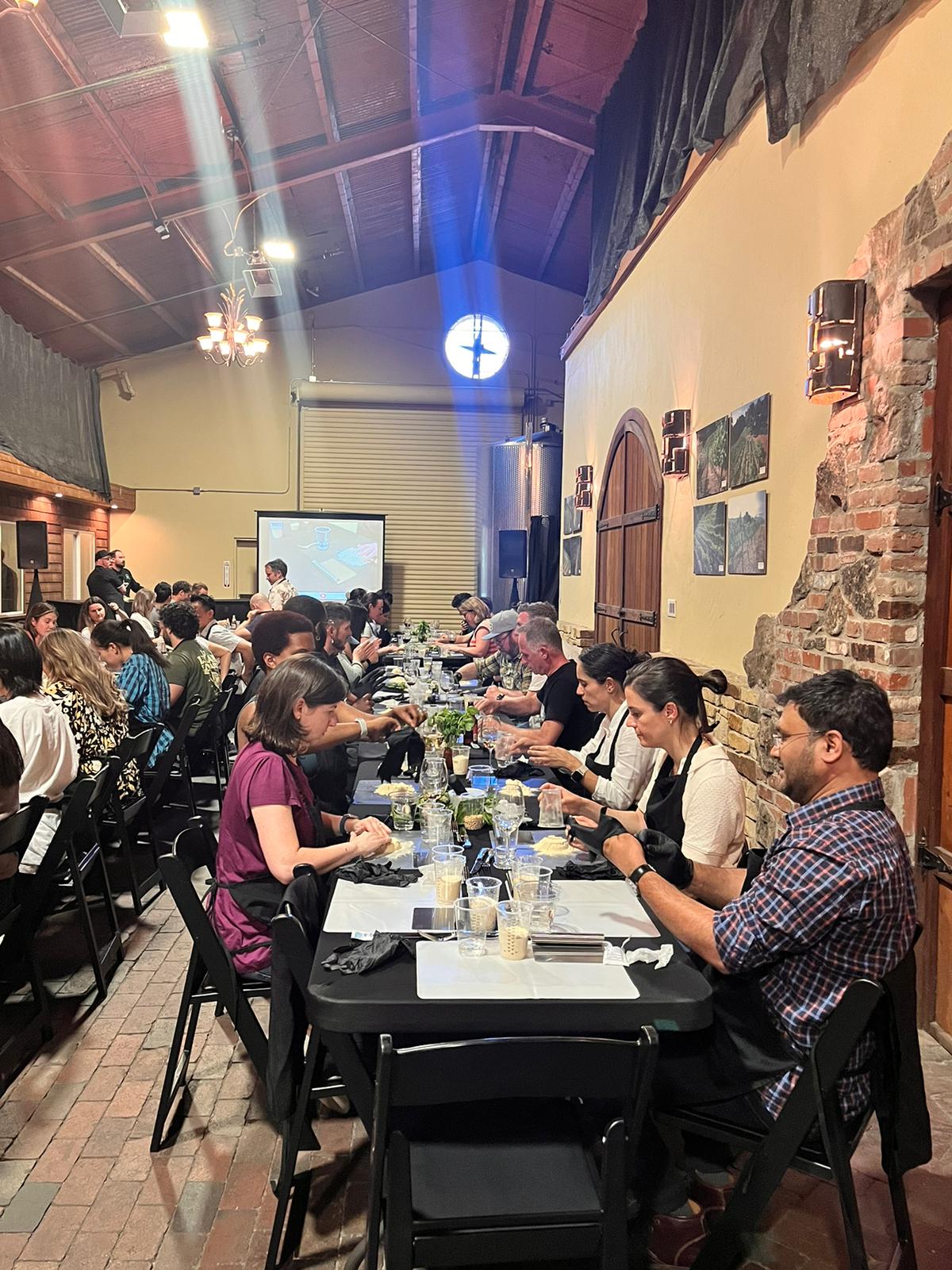 Guests seated along a long banquet table in a rustic venue lit with blue stage lighting