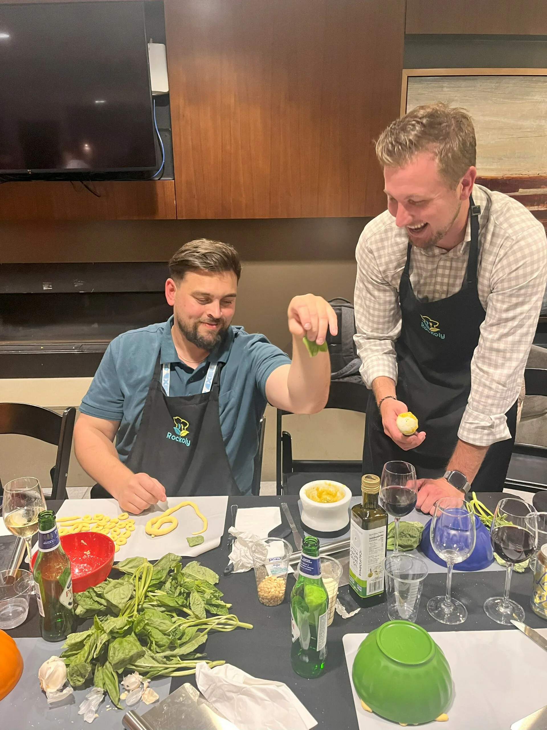 Two guests in aprons laugh while squeezing lime and prepping vegetables at a cooking event