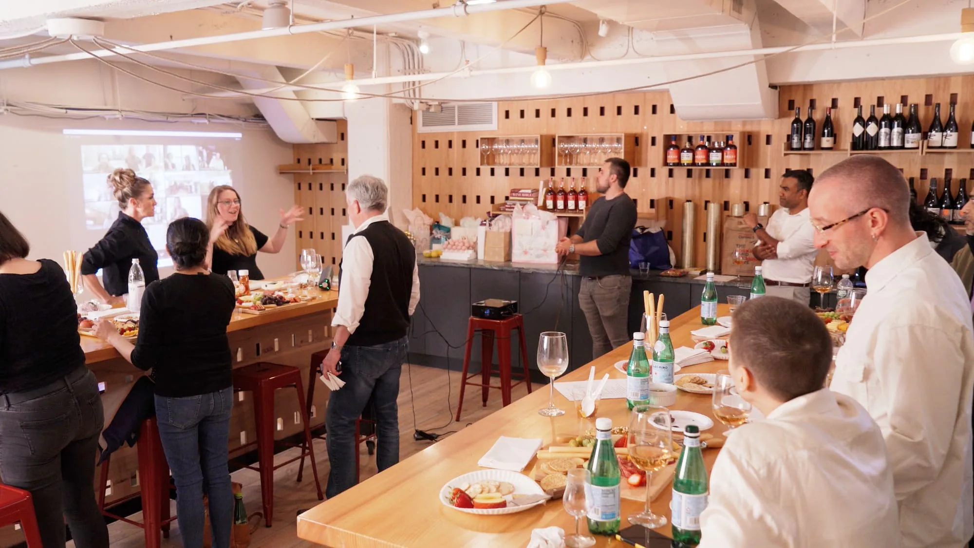 Guests mingling over food and drinks at a long counter in a loft space lined with wine bottle racks