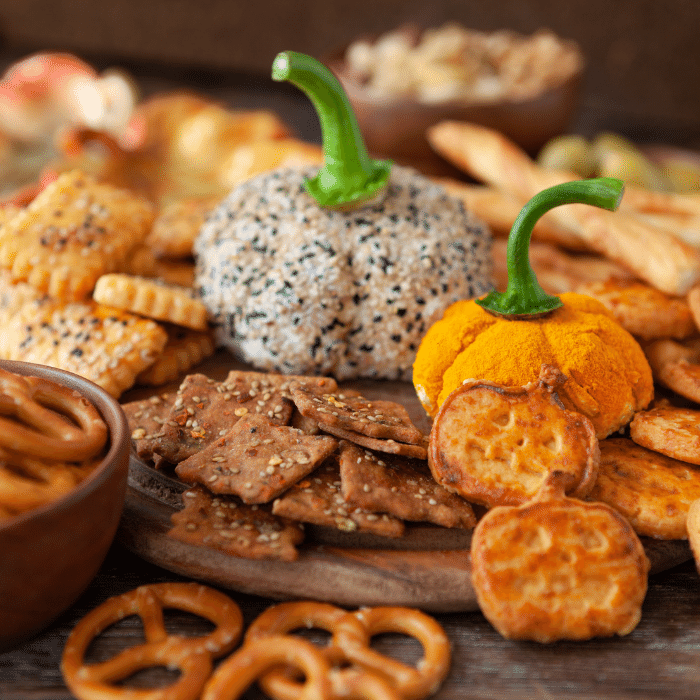 Halloween snack board with two pumpkin-shaped cheese balls, crackers, pretzels and breadsticks