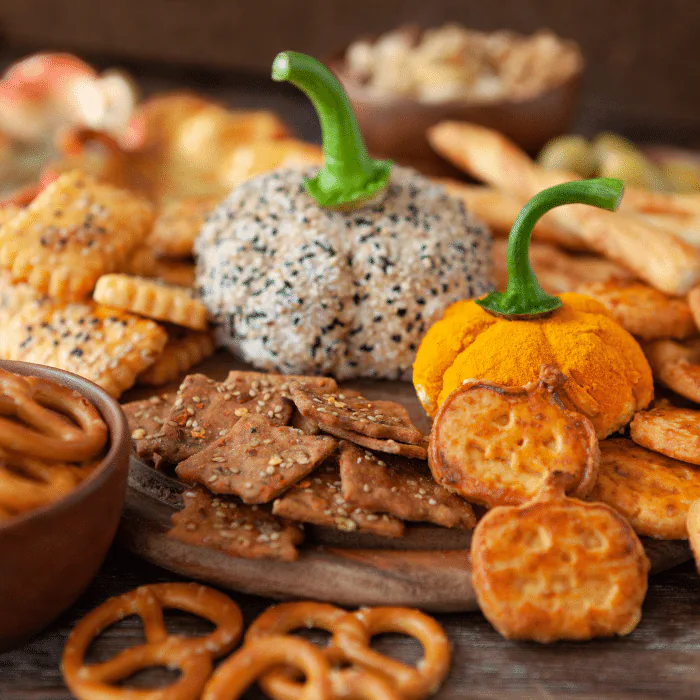 Halloween snack board with two pumpkin-shaped cheese balls, crackers, pretzels and breadsticks