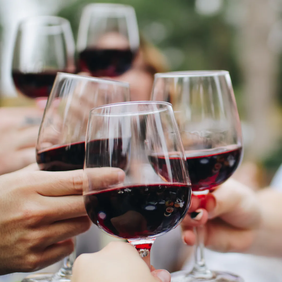Several hands clinking glasses of red wine together in a toast