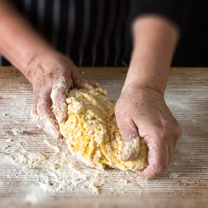 Floured hands kneading a mound of golden egg pasta dough on a wooden board