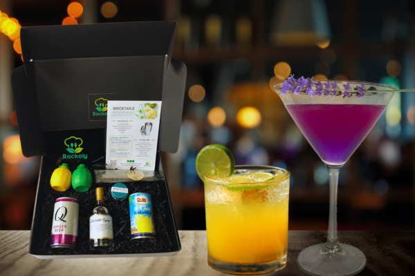 Cocktail kit box with mini bottles beside a purple lavender cocktail and an orange pineapple drink