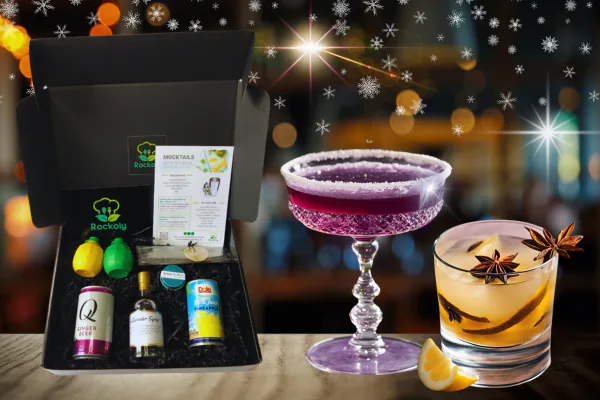 Cocktail kit box holding a Mocktails recipe card, ginger beer, pineapple juice and syrup, with two finished drinks