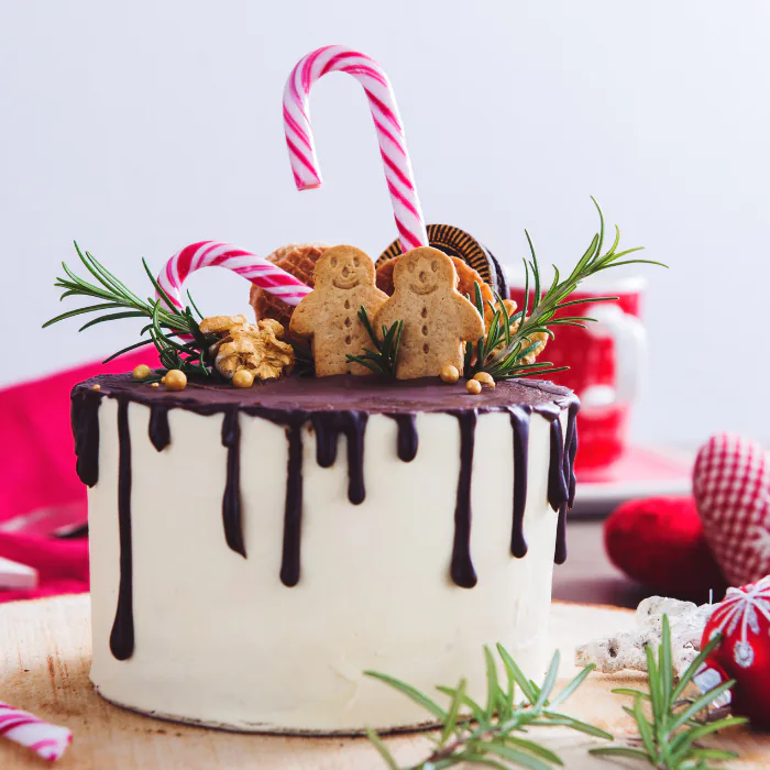 Layer cake with chocolate drip icing topped with gingerbread men, candy canes and rosemary