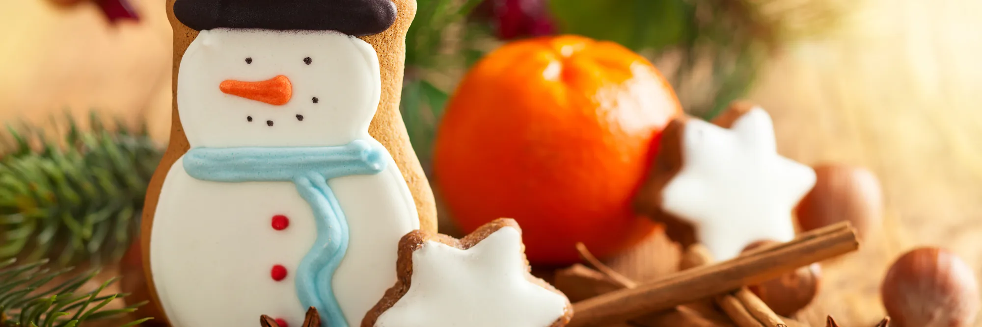 Iced snowman cookie beside cinnamon star cookies, a clementine and pine sprigs on a festive table