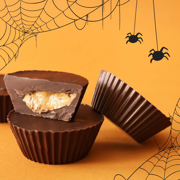 Homemade chocolate peanut butter cups, one cut open, on an orange background drawn with spiderwebs