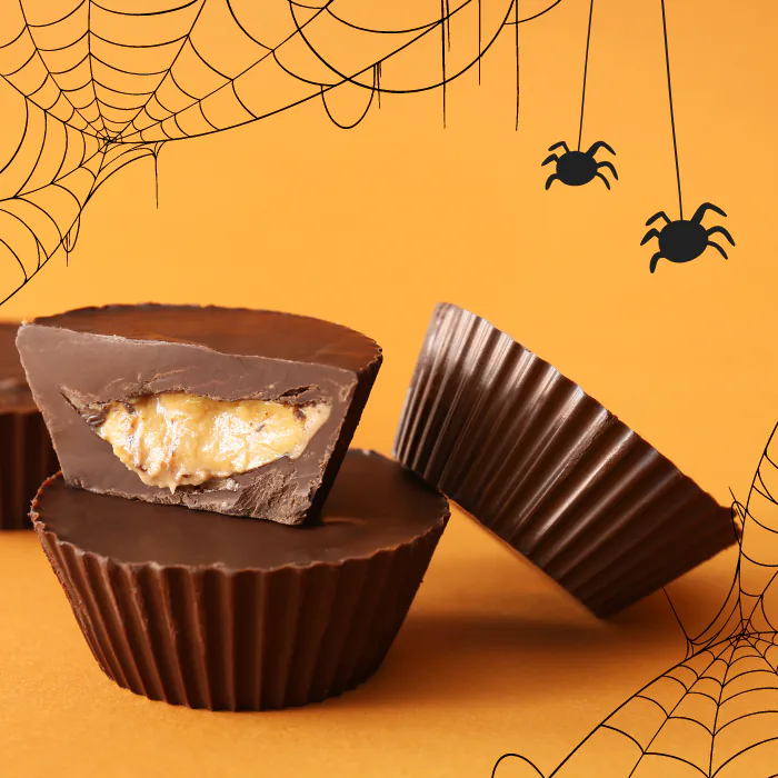 Homemade chocolate peanut butter cups, one cut open, on an orange background drawn with spiderwebs
