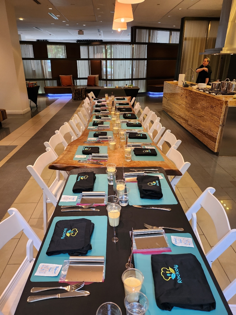Long banquet table set with teal placemats, folded aprons and glasses in a hotel dining room