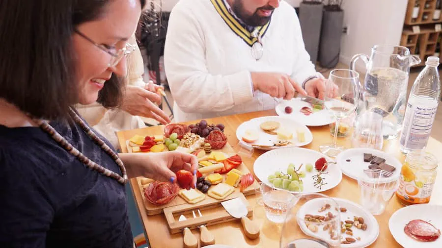 Guests around a table sharing charcuterie boards of cured meats, cheese, grapes and chocolate