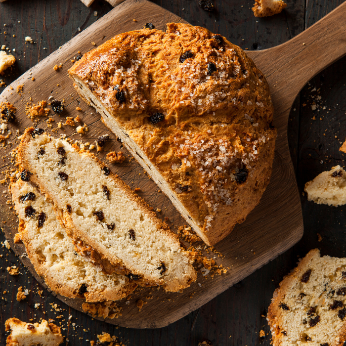 Round raisin-studded Irish soda bread, part of it sliced, on a wooden board