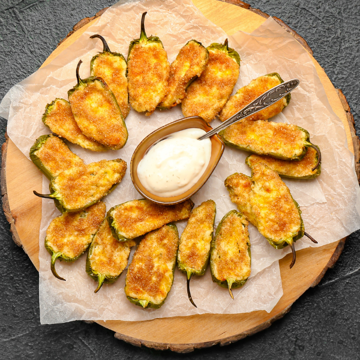 Breaded jalapeño poppers arranged in a ring around a bowl of creamy dip on a wooden board