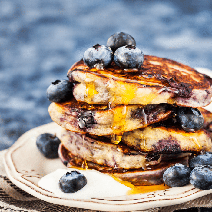 Stack of blueberry pancakes topped with fresh blueberries and syrup on a plate