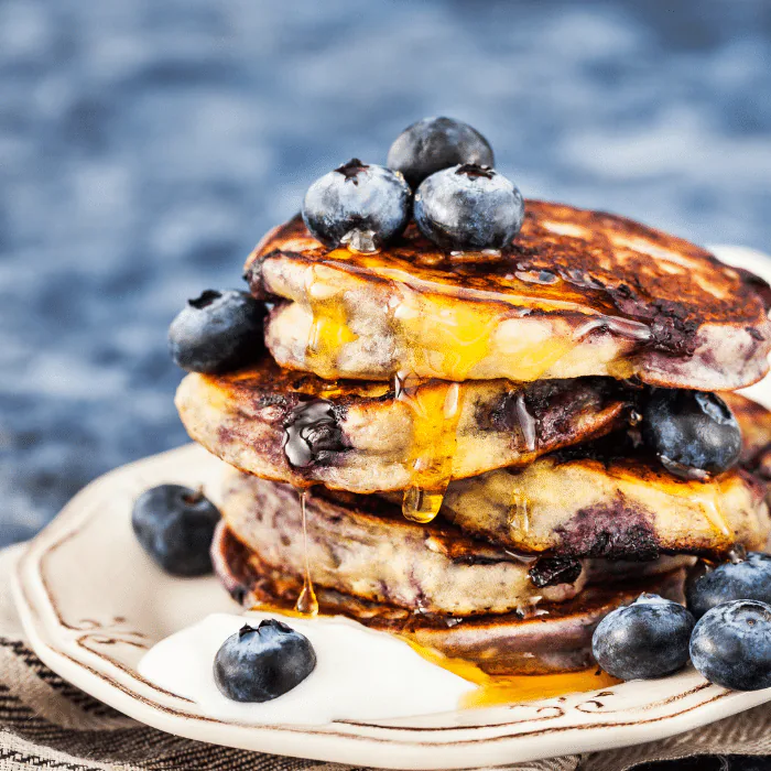 Stack of blueberry pancakes topped with fresh blueberries and syrup on a plate