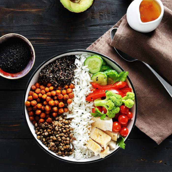 Buddha bowl sectioned with lentils, chickpeas, quinoa, rice, tofu, broccoli, cucumber and tomatoes