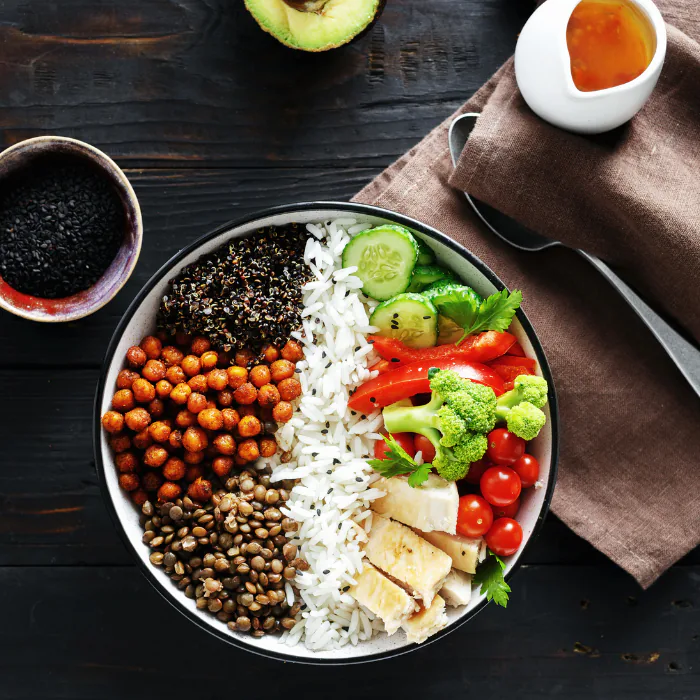 Buddha bowl sectioned with lentils, chickpeas, quinoa, rice, tofu, broccoli, cucumber and tomatoes