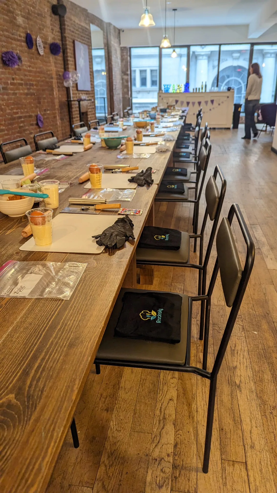 Long wooden table in a brick loft laid with place settings, bowls and folded aprons on each chair
