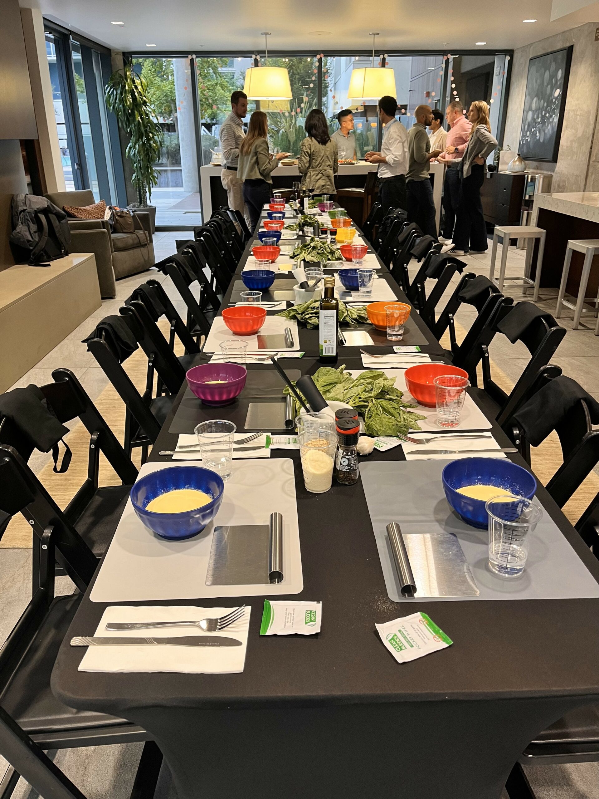 Long table set with colorful bowls of ingredients and place settings as guests gather at the far end