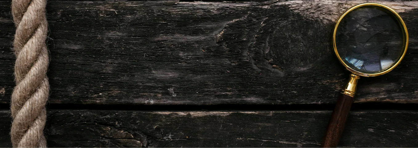 Brass magnifying glass and coiled rope on dark weathered wood planks
